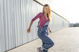 Happy blonde woman wearing casual clothes dancing a modern urban dance outdoors in the street