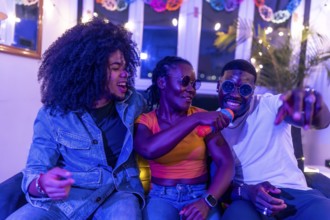 Happy people singing karaoke during night party sitting on a sofa and laughing