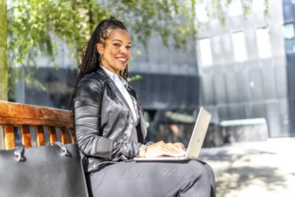 Side view portrait of a successful latin businesswoman working with laptop sitting on city bench