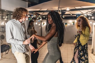 Multi-ethnic friends dancing holding hands latin music at night party in a terrace