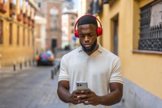 Frontal portrait of a serious young african man using mobile phone and headphones walking down
