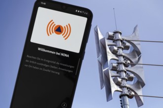 (Photomontage) Close-up of a siren at a school, next to it the open warning app NINA on a