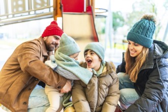 Family enjoying a winter day at the playground, bundled up in warm clothes and laughing together