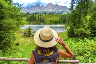 Female tourist wearing straw hat enjoying the landscape of lake carezza with latemar mountain range