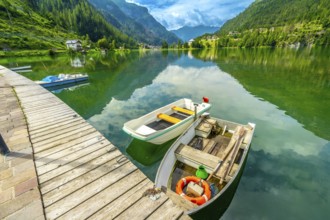 Wooden pier with boats reflecting in the emerald waters of alleghe lake with the dolomites in the