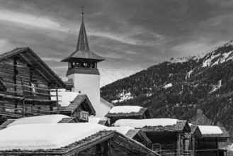 Old wooden houses with snow-covered roofs and the Saint Theodule church in the historic village