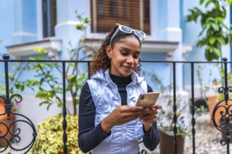 Urban young african american woman using phone sitting in the street next to a colorful building