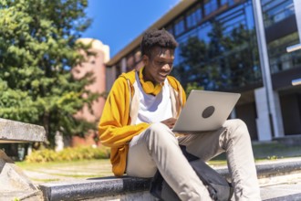African man sitting at staircases on the university campus studying using laptop