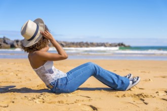 Side view of an unrecognzizable latin woman in summer denim clothes sitting on a beach gazing the