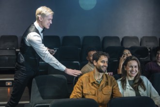 Movie theater usher guiding spectators to their seats and checking tickets, ensuring a smooth movie