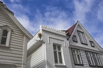 View upwards to white wooden houses with striking architecture under a clear blue sky, Bergen,