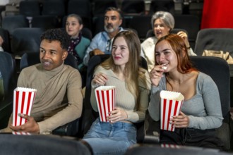 Group of friends watching a film at the movie theatre, eating popcorn and enjoying their leisure