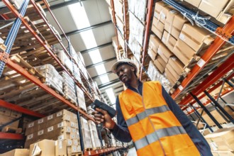 Low angle view of an african manual worker scanning packages to deliver in a warehouse