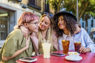 Cute female friends embracing while drinking sodas and eat snacks in an outdoor terrace