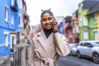 Happy young african american businesswoman using phone walking in the city along a colorful street