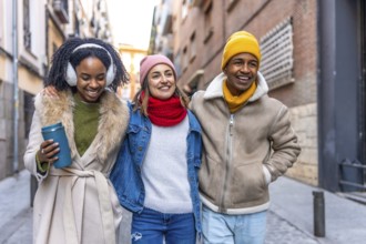 Happy multi ethnic friends are enjoying a winter day together, walking arm in arm through a city