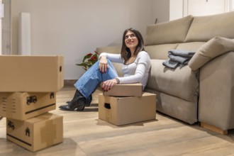 Young woman taking a break from unpacking, sitting on the floor of her new apartment and looking up