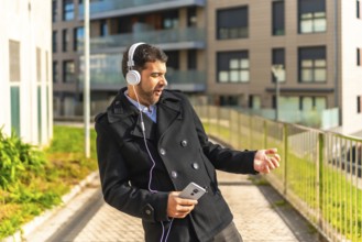 Adult caucasian businessman in casual winter clothes dancing while listening to music with mobile