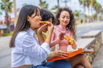 Multi-ethnic women sitting in the city enjoying a take away pizza together