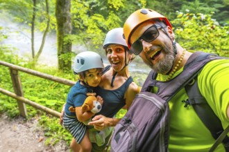 Happy family wearing helmets taking a selfie while hiking on a trail next to a river in vintgar