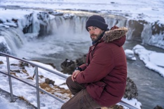 Portrait of a man hiker at frozen Godafoss waterfall at sunset in winter, Iceland, Europe