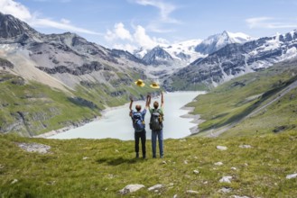Two friends throwing yellow hats in the air, mountaineers in front of a blue mountain lake, Lac des