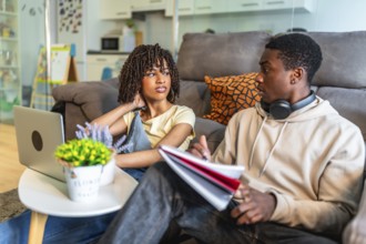 Two college students discussing homework, using laptop and notebooks, sitting on floor at home