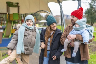 Happy family enjoying a delightful winter day at the playground, bundled up in warm clothes,
