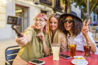 Three multi-ethnic women gesturing success while taking selfie with camera at bar