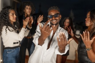 Brunette cool man in sunglasses gesturing while dancing surrounded by friends at night in a city