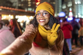 Smiling young woman wearing yellow winter clothes taking a selfie at a christmas market showing