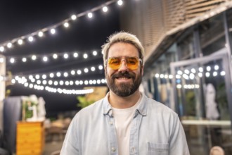 Hipster caucasian man with modern sunglasses smiling in a bar terrace at night