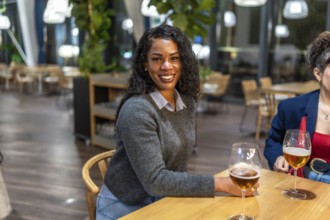 Latin woman smiling at camera sitting on a bar terrace with friends enjoying fresh beer