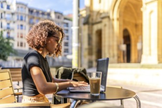 Arab young businesswoman working on remote in a sidewalk cafeteria in the main square of a city