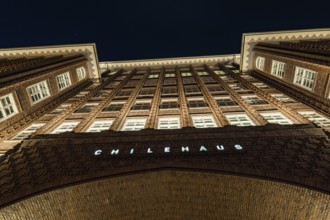 Symmetrical inner courtyard of a Kontorhaus at night, rows of windows and brick façade illuminated,