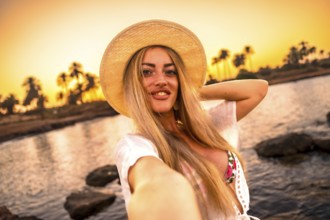 Personal point of view of a blonde woman smiling at camera while taking selfie during tropical