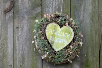 A heart-shaped welcome sign in a wreath with flowers, attached to a wooden surface, North