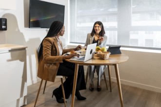 Two businesswomen are enjoying breakfast and working on a laptop during their business trip,