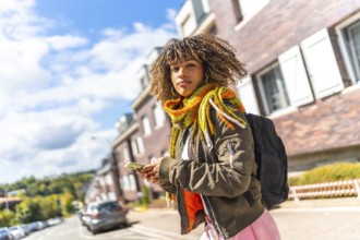 Vital young woman turning to look at camera while using phone in the city