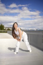 Vertical full length photo of a caucasian young female artist performing urban dance on a bridge
