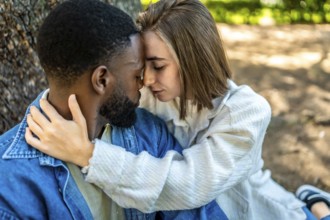 Close-up side top view of a romantic multiracial couple embraced sitting on a park