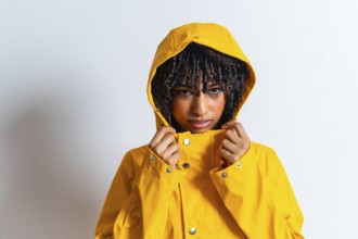 Studio portrait of a young woman tightening her yellow raincoat hood, getting ready for bad weather