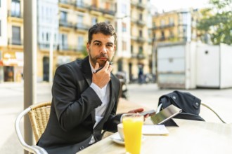 Thoughtful businessman gesturing hand on chin while working using mobile phone and digital tablet