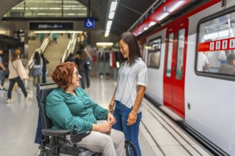 Disabled woman in wheelchair and friend talking while waiting in the platform of the metro