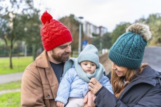 Smiling parents holding their baby wearing warm winter clothes and enjoying a winter day outdoors