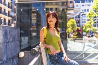 Portrait of a cool asian female young skater leaning on rail in the city