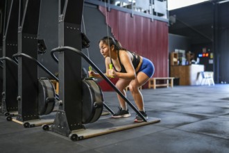 Full length photo of an asian strong woman pulling down weights using lat machine in a gym
