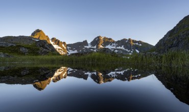 Rocky mountain peaks reflected in a small pond, mountain landscape with alpenglow at sunrise, at