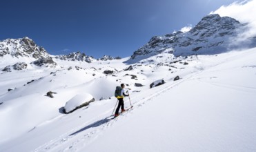 Ski tourers ascending through picturesque snow-covered mountain landscape with Piz Kesch summit,