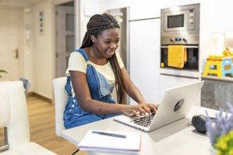 Young student concentrating on her studies, typing on a laptop in a modern kitchen, demonstrating
